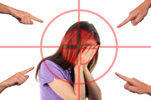 Chica cubriéndose la cara señalada por varias manos, representación del acoso escolar y el señalamiento social